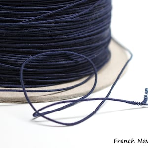 May include: A spool of dark blue elastic cord, also known as stretch cord or beading cord. The cord is wound around a cardboard spool and a length of cord is hanging off the spool.