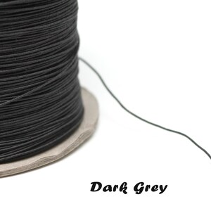 Puede incluir: Un carrete de cordón elástico gris oscuro, enrollado alrededor de un núcleo de cartón. El cordón es delgado y flexible, y es ideal para hacer joyas u otras manualidades.