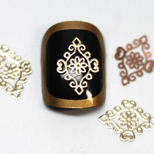 May include: Four gold-coloured metal nail art embellishments in a diamond shape with a floral design. The embellishments are on a white surface.