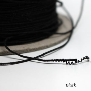 May include: A spool of black elastic cord, with a length of cord extending from the spool. The cord is twisted and knotted.