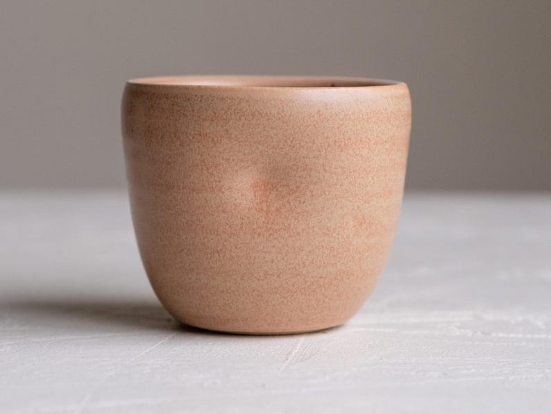 Pu&ograve; includere: Una tazza in ceramica di colore pesca chiaro con forma arrotondata e superficie testurizzata.