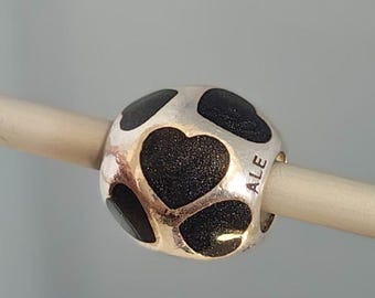 May include: A spherical silver charm bead featuring a repeating pattern of recessed black glittery heart shapes. The metal surface is polished silver, and the side of the bead is clearly engraved with the letters ALE in a clean, sans-serif font.
