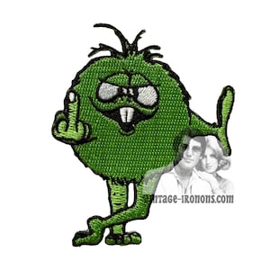 May include: Green fuzzy monster with a toothy grin giving the middle finger. The monster has two legs and is standing on a white background.