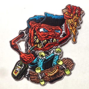 May include: An embroidered patch featuring a red, cartoon monster with a blue hat, holding a pizza slice in one hand and a skateboard in the other. The monster has a toothy grin and is wearing a blue and white shirt. The patch is on a white background.