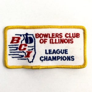 Puede incluir: Un parche blanco bordado con un borde amarillo. El parche presenta una letra estilizada "B" y "C" en azul y rojo con una "I" roja dentro de la "C". El texto "Bowlers Club of Illinois League Champions" está bordado en rojo en el parche.