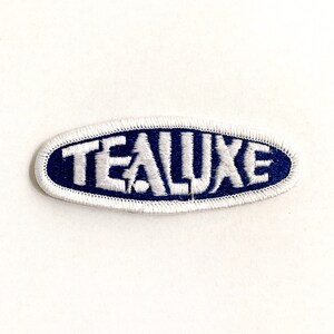 May include: White embroidered patch with the word "Tealuxe" in a blue oval.