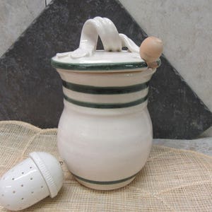 May include: White ceramic tea pot with a green striped design and a wooden knob on the lid. The pot has a handle and comes with a separate white ceramic tea infuser.