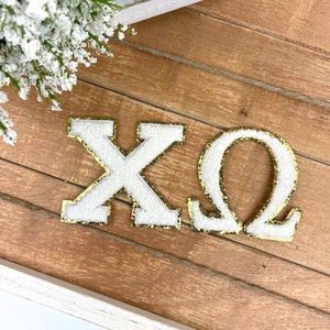 May include: White felt letters with gold glitter trim spelling "XO" on a wood background.