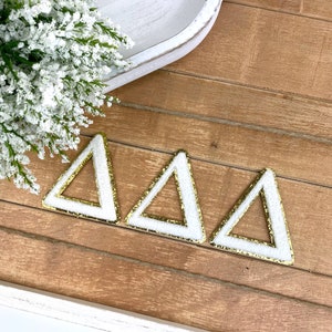 May include: Three white triangle-shaped ornaments with gold glitter trim.