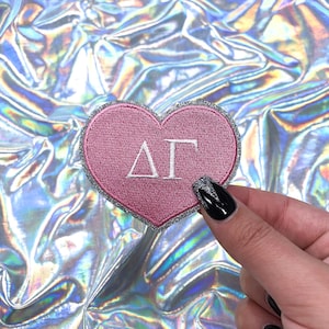 May include: Pink heart-shaped patch with silver glitter trim and white embroidered letters "ΔΓ"