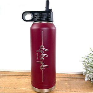 May include: A maroon stainless steel water bottle with a black lid and a straw. The bottle has a silver band around the bottom and the words "alpha phi est. 1872" engraved on the side.