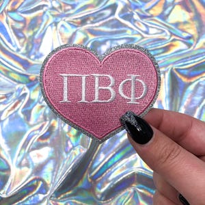 May include: Pink heart-shaped patch with silver glitter trim and white embroidered letters spelling "ПВФ".