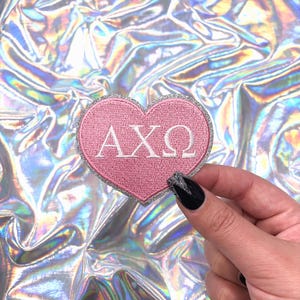 May include: Pink heart-shaped patch with silver glitter trim and the letters AXQ in white.