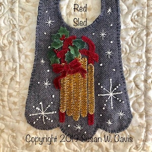 Könnte beinhalten: Ein grauer Filz-Weihnachtsanhänger mit einem roten Schlitten und einem Stechpalmen-Design. Der Anhänger hat oben ein Loch zum Aufhängen und der Text "My Red Sled" ist auf der Vorderseite gestickt. Copyright 2019 Susan W. Davis.