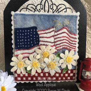 May include: Wool appliqu&eacute; of an American flag with fireworks and daisies, with the text "Daisy Wave" and "Wool Appliqu&eacute;" and "Copyright 2020 Susan W Davis".