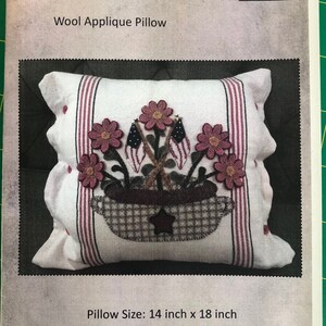 K&ouml;nnte beinhalten: Ein wei&szlig;es Woll-Applikationskissen mit einem Design aus einem Blumenkorb und Flaggen. Das Kissen ist 14 Zoll mal 18 Zoll gro&szlig;. Der Text "Summer Blooms" ist auf der Vorderseite des Kissens aufgedruckt.