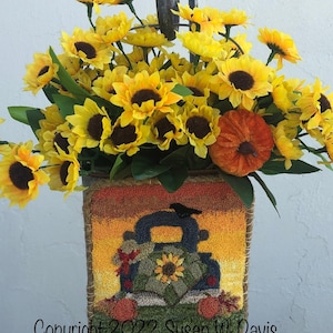 May include: A rustic-style, burlap-covered planter with a hand-stitched design of a vintage truck carrying pumpkins and sunflowers. The planter is filled with a bouquet of yellow sunflowers and a small orange pumpkin.