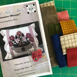 K&ouml;nnte beinhalten: Ein Bastelset f&uuml;r ein Woll-Applikationskissen mit einem Blumendesign mit dem Titel "Summer Blooms" und Anleitungen zur Herstellung eines Kissens mit den Ma&szlig;en 35,5 cm x 45,7 cm. Das Set enth&auml;lt Stoffreste in verschiedenen Farben, Kn&ouml;pfe und einen goldenen Stern.