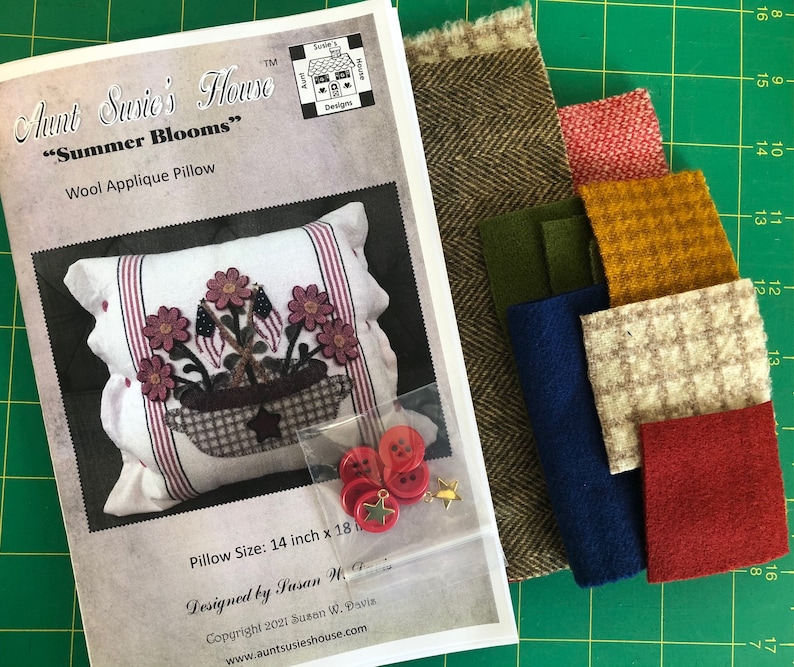 K&ouml;nnte beinhalten: Ein Bastelset f&uuml;r ein Woll-Applikationskissen mit einem Blumendesign mit dem Titel "Summer Blooms" und Anleitungen zur Herstellung eines Kissens mit den Ma&szlig;en 35,5 cm x 45,7 cm. Das Set enth&auml;lt Stoffreste in verschiedenen Farben, Kn&ouml;pfe und einen goldenen Stern.