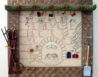 May include: A framed Christmas-themed artwork featuring a fireplace scene with stockings, skis, and a miniature shovel. The frame is brown with a textured pattern. A garland with red berries and green leaves adorns the top.
