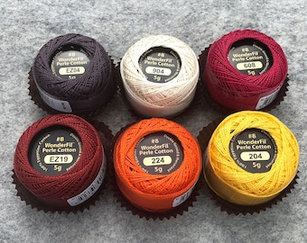 May include: Six spools of WonderFil Perle Cotton embroidery thread in various colors, including red, orange, yellow, white, and brown. Each spool is labeled with the brand name, thread number, and weight (5g).