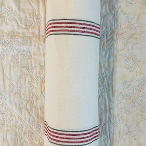 May include: A rolled up white fabric with red and black stripes. The fabric is folded and rolled up, with the stripes visible on the ends.