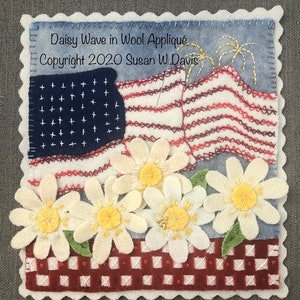 May include: A wool applique artwork featuring a red, white, and blue American flag with a wave design. The flag is surrounded by white daisies with yellow centers. The background is a red and white gingham pattern. The artwork is titled "Daisy Wave in Wool Applique" and is copyrighted 2020 by Susan W. Davis.