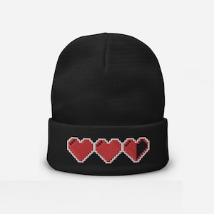 May include: Black knit beanie with a red pixelated heart design. The hearts are in a row and the last heart is half filled.