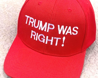 May include: A bright red baseball cap with the embroidered text "TRUMP WAS RIGHT!" in white. The cap has a curved brim and a button on top. The hat is made of a sturdy fabric.