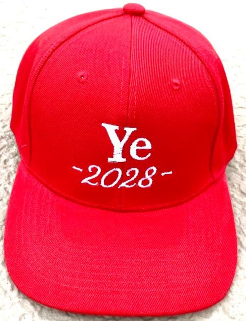 May include: A bright red baseball cap with a curved brim. The cap features the white text "Ye -2028-" embroidered on the front. The cap has a button on top and a structured design.