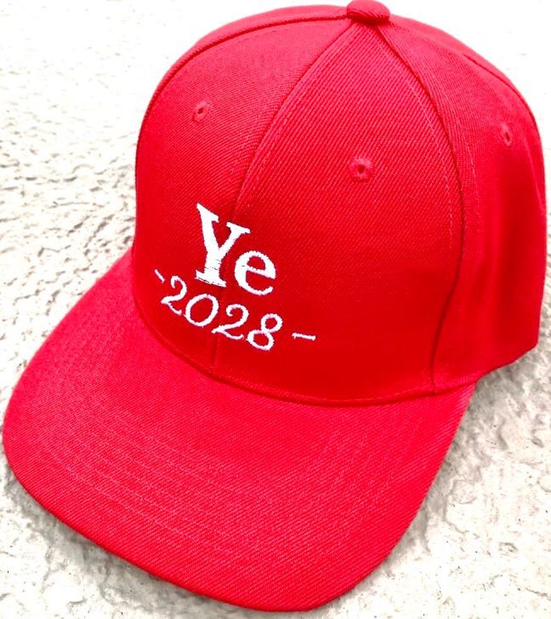 May include: A bright red baseball cap with the word "Ye" and the year "2028" embroidered in white. The cap has a curved brim and a rounded top.