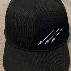 May include: A black baseball cap with a white embroidered design of four arrows pointing to the right.