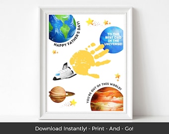 May include: A framed print with a space theme, featuring a yellow handprint, planets, a rocket, and the text "Happy Father's Day!" and "To the Best Dad in the Universe!" The artwork is in watercolor style with a white frame.