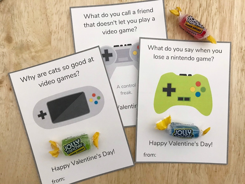 May include: Three Valentine's Day cards with gaming-themed jokes and candy. One card features a gray handheld console graphic, another a gray controller, and the third a green controller. Each card has a Jolly Rancher candy.