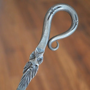 May include: A silver metal fireplace poker with a decorative handle shaped like a face with a beard and a star design.