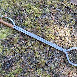 May include: A long, black metal fireplace tool with a leather handle. The tool has two loops at one end and a large, round loop at the other end.