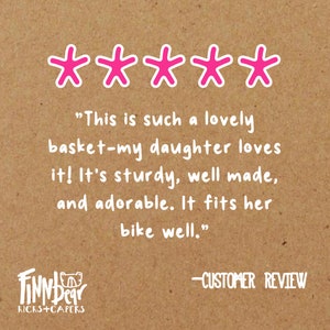 May include: A customer review on a brown background with five pink star icons. The text reads: "This is such a lovely basket-my daughter loves it! It's sturdy, well made, and adorable. It fits her bike well."