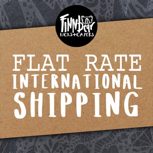 May include: A brown card with the words "FLAT RATE INTERNATIONAL SHIPPING" in large white letters. A black circle at the top contains the text "FINN BEAR KICKS + CAPERS" in white.