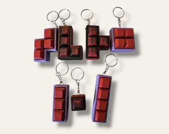 Peut inclure: Cinq porte-clés en forme de Tetris de différentes couleurs. Les porte-clés sont en plastique et ont une finition mate. Les porte-clés sont en forme de blocs Tetris, chaque bloc ayant une couleur différente. Les porte-clés sont attachés à des anneaux de clés argentés.