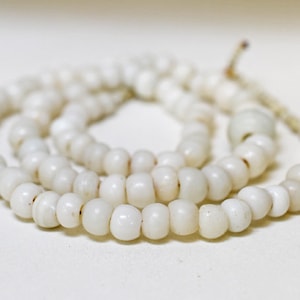 Puede incluir: Un collar de cuentas blancas con un diseño sencillo. Las cuentas son redondas y lisas, y el collar está enhebrado en un cordón delgado.