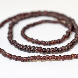 May include: A long strand of dark brown beads, strung together to form a necklace. The beads are small and uniform in size, creating a simple and elegant look.