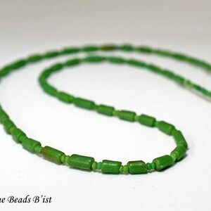 Puede incluir: Una hebra de cuentas de vidrio verde, enhebradas en un hilo blanco. Las cuentas son de forma rectangular y tienen una superficie ligeramente irregular.