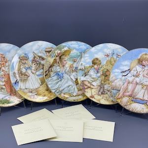 Peut inclure: Ensemble de cinq assiettes en porcelaine décoratives représentant des enfants sur une plage. Chaque assiette représente une scène différente avec un schéma de couleurs bleu et blanc. Les assiettes sont exposées sur des supports avec des certificats d'authenticité.
