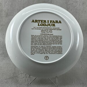 May include: A white ceramic plate with a gold border and text in Swedish. The text reads "Arter i Fara Lodjur" (Species in Danger Lynx) and includes information about the European wildcat and the lynx. The plate is part of a series of collector's plates.