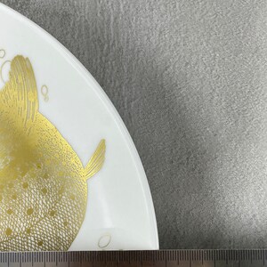 May include: A white ceramic plate with a gold-colored fish design. The plate is 25 inches in diameter.