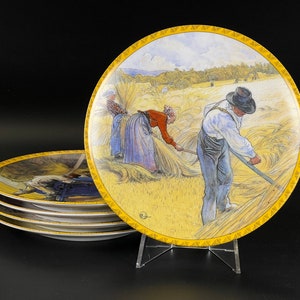 May include: Set of decorative plates featuring a pastoral scene of people harvesting wheat. The plates have a yellow border with a repeating design. The artwork depicts figures in a field, with a blue sky and trees in the background.