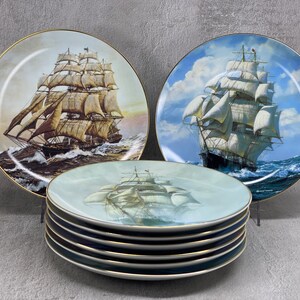 May include: A set of eight decorative plates featuring a vintage sailing ship with a blue and white background. The plates are stacked on top of each other and have a gold rim.