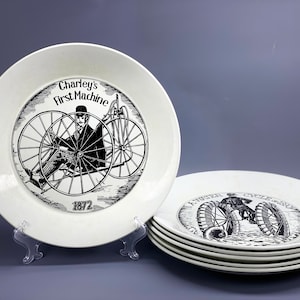 May include: A set of six white ceramic plates with black and white illustrations of a man riding a bicycle. The plates feature the text "Charley's First Machine 1872" and "Water Cycle 1880".