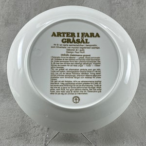 May include: A white ceramic plate with a gold border and text in Swedish. The text describes the gray seal, a species of seal found in the Baltic Sea. The plate is part of a series of collector's plates.
