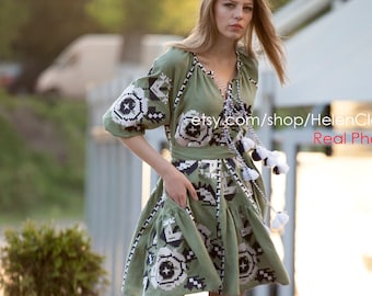 May include: A woman wearing a green embroidered dress with white and black geometric patterns. The dress has a V-neckline and short sleeves. She is standing on a sidewalk with a green bush in the background. The text "etsy.com/shop/HelenCloth Real Photo" is visible on the image.